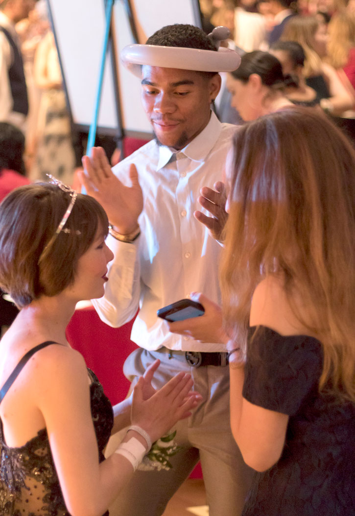 Student-athlete (balloon animal on his head) dances with young women.