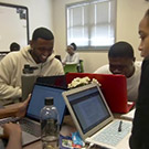 Students sit around a table with laptops.