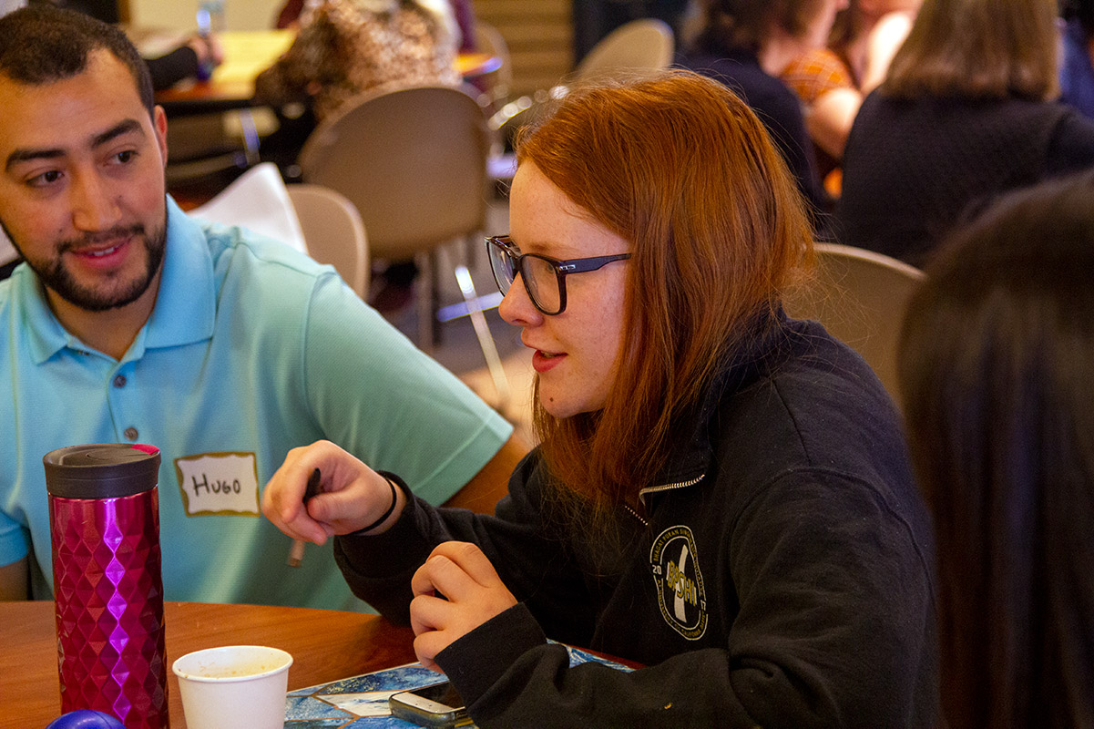 Woman sits at table, talking to others.