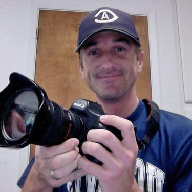 Man in CA ballcap, holding camera.