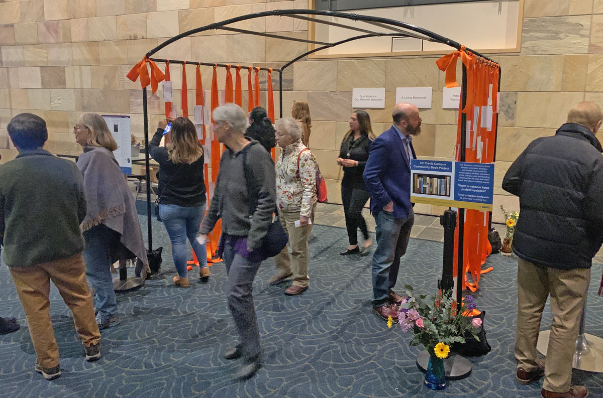 orange ribbons with tags attached, hanging from metal structure, with a dozen people viewing.