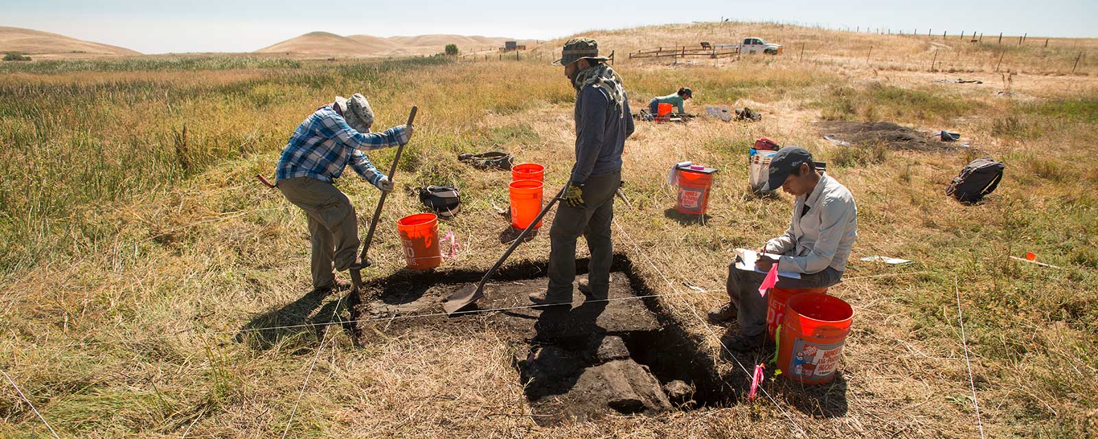 three students in heavy clothes working on a plot in a big field