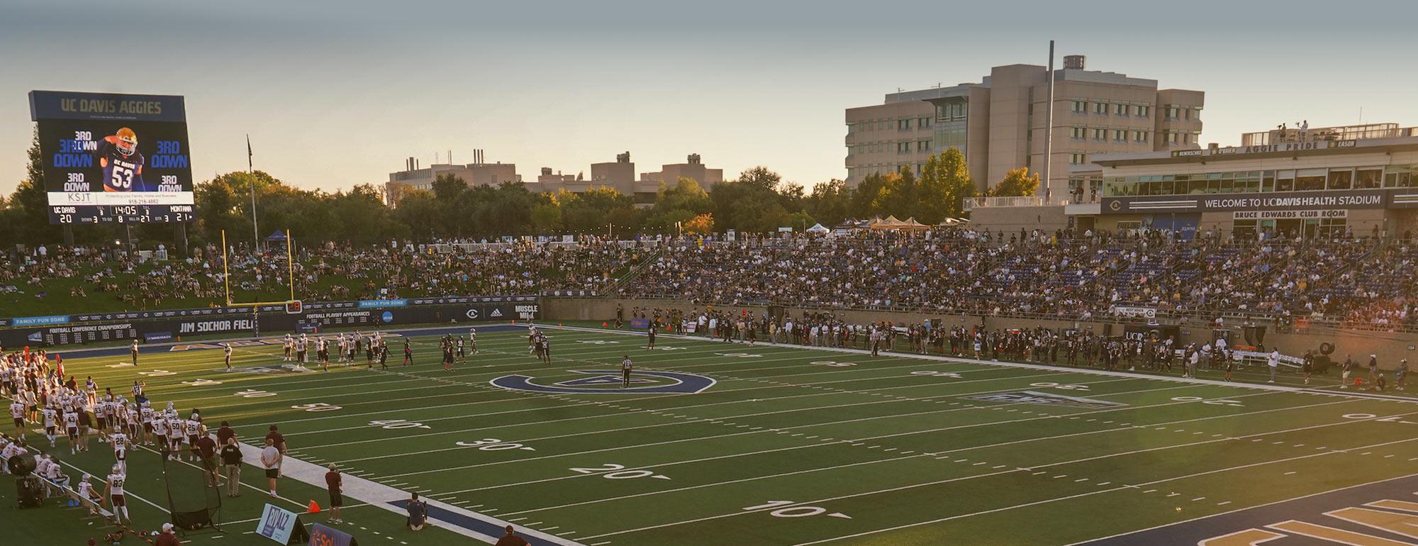 Panoramic football stadium at sunset, teams on the field and packed stands