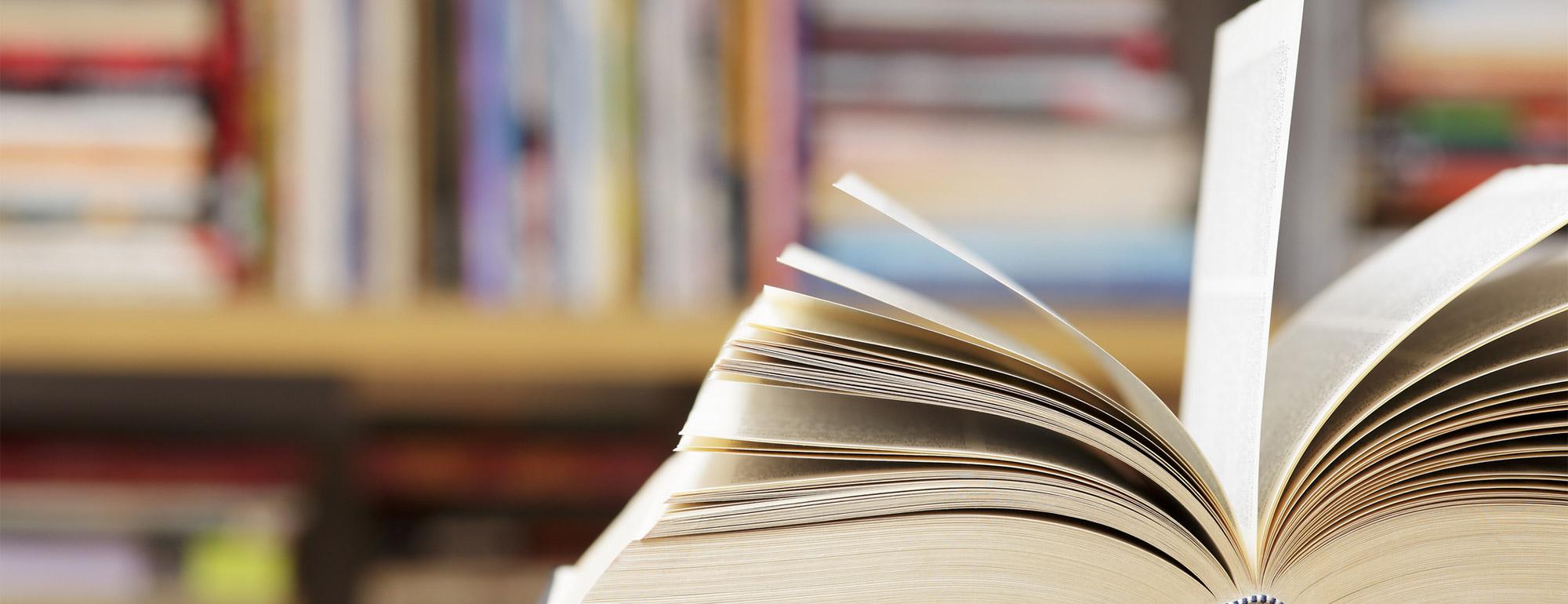 A close up of a book with pages turning and books on shelves in the background