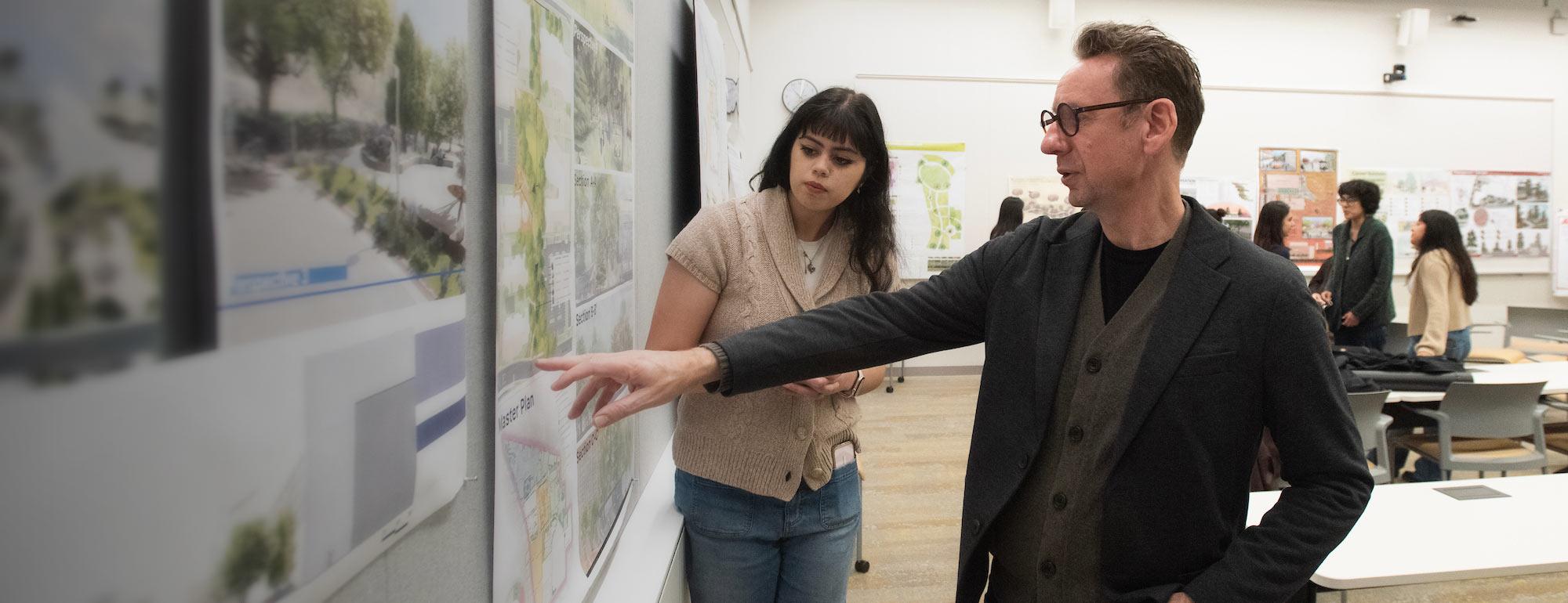 Two designers in studio pointing at pinned architectural drawings
