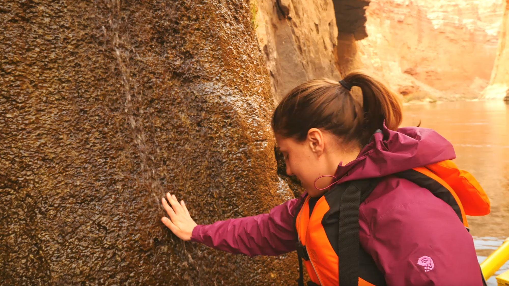 A student researcher on a trip to the grand canyon puts her hand in a waterfall in the canyon