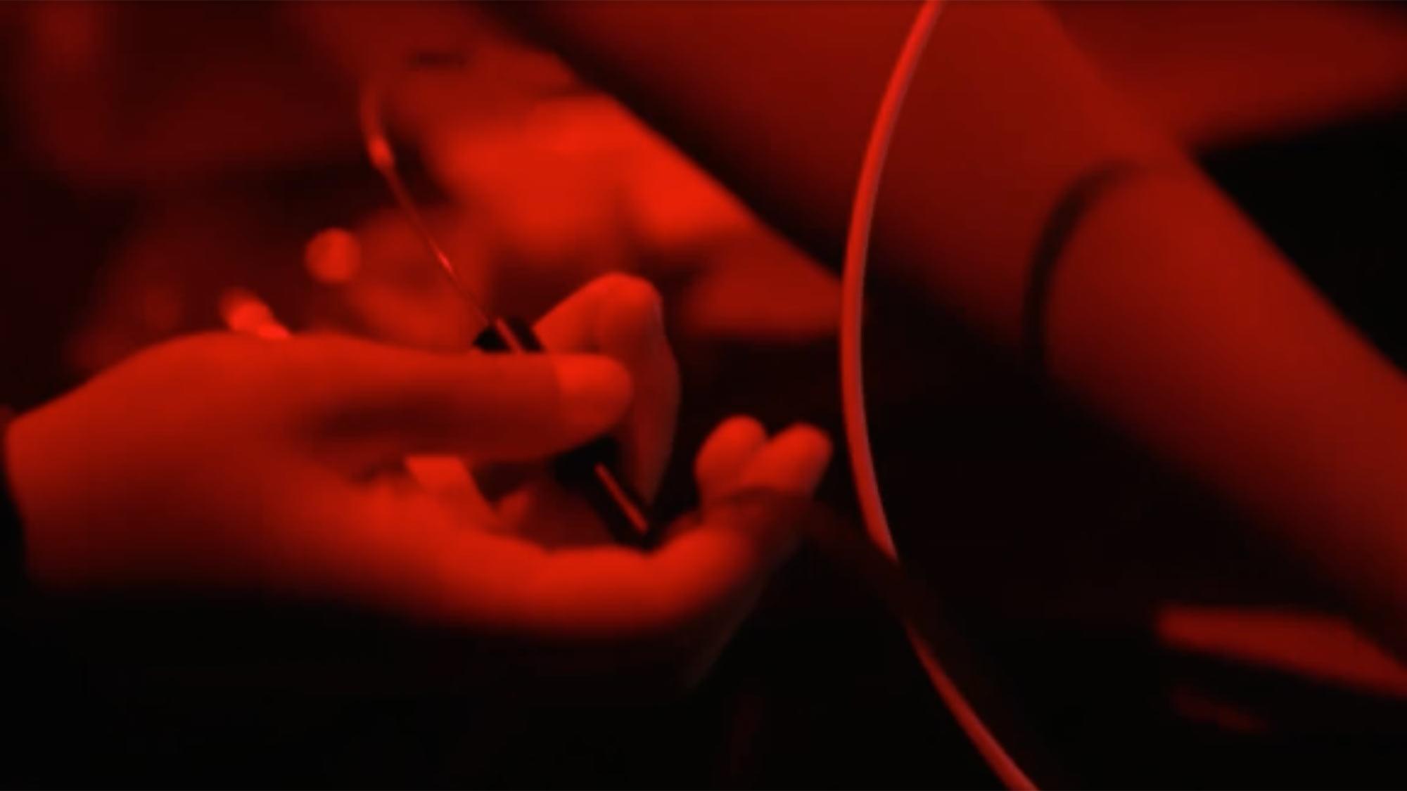 Hands in red light holding a syringe near an outstretched arm