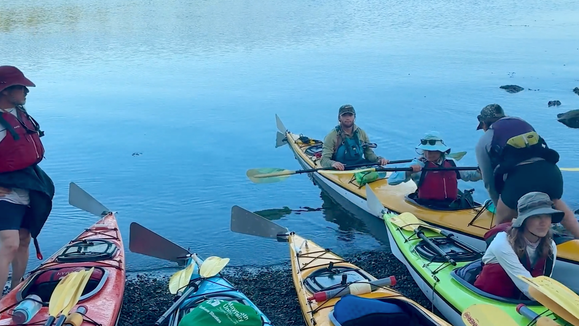Group of kayakers in colorful kayaks on calm blue water, wearing life jackets