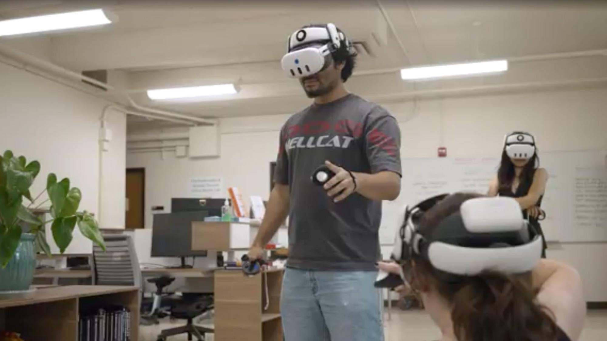 Man in office wearing VR headset and holding controllers, colleagues using headsets