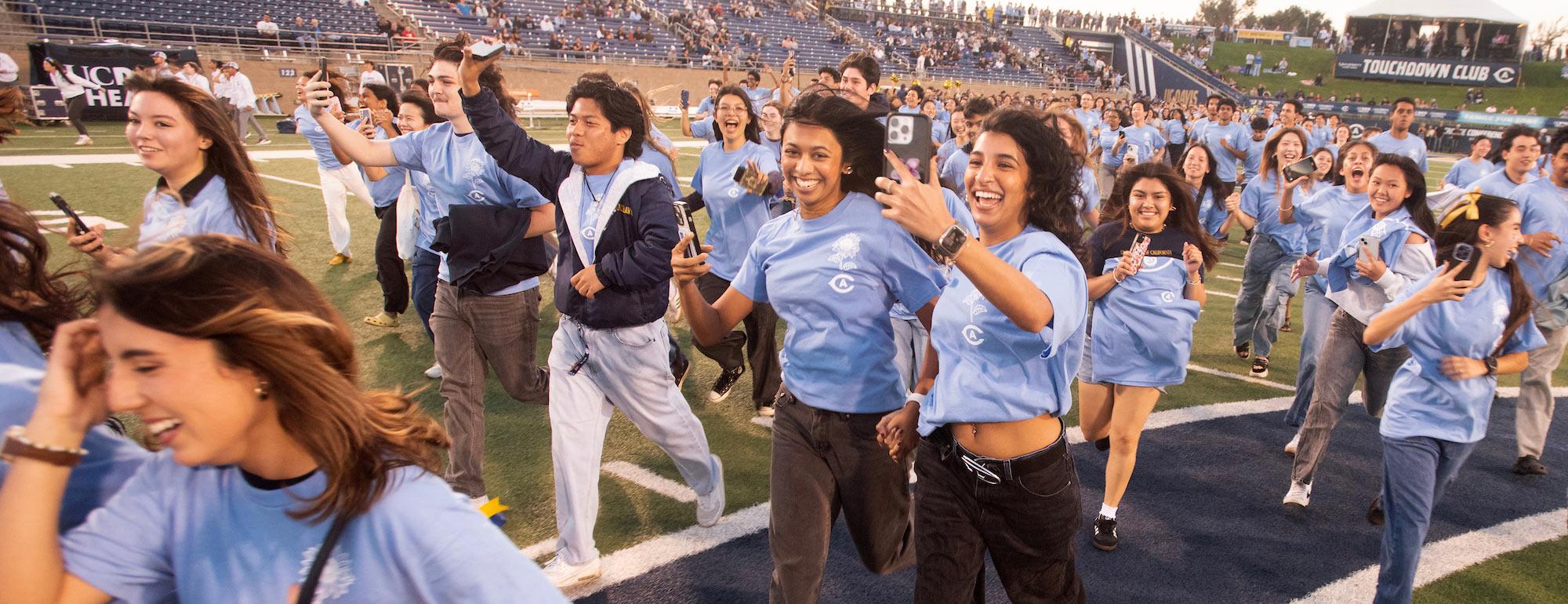 Smiling young people in light blue shirts running across a stadium field