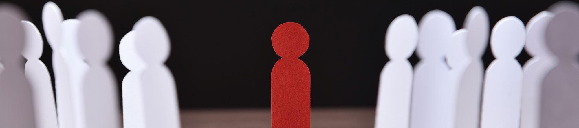 Red paper cutout standing between white cutout figures on dark background