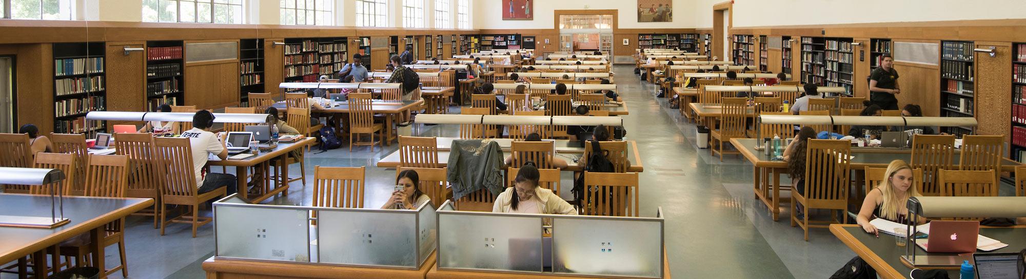 Empty library reading room with rows of wooden tables, chairs and tall windows