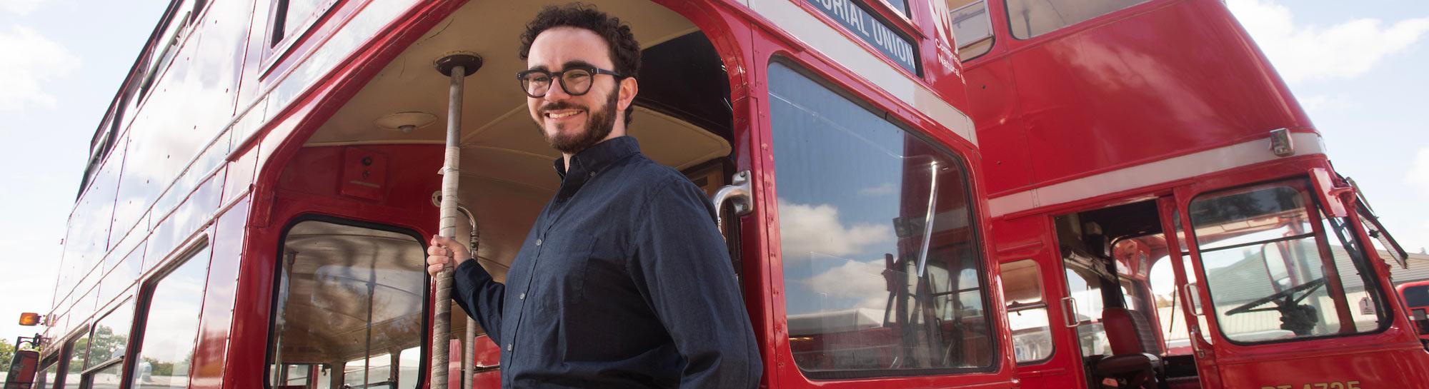 Smiling bearded man with backpack and glasses boarding red double-decker bus
