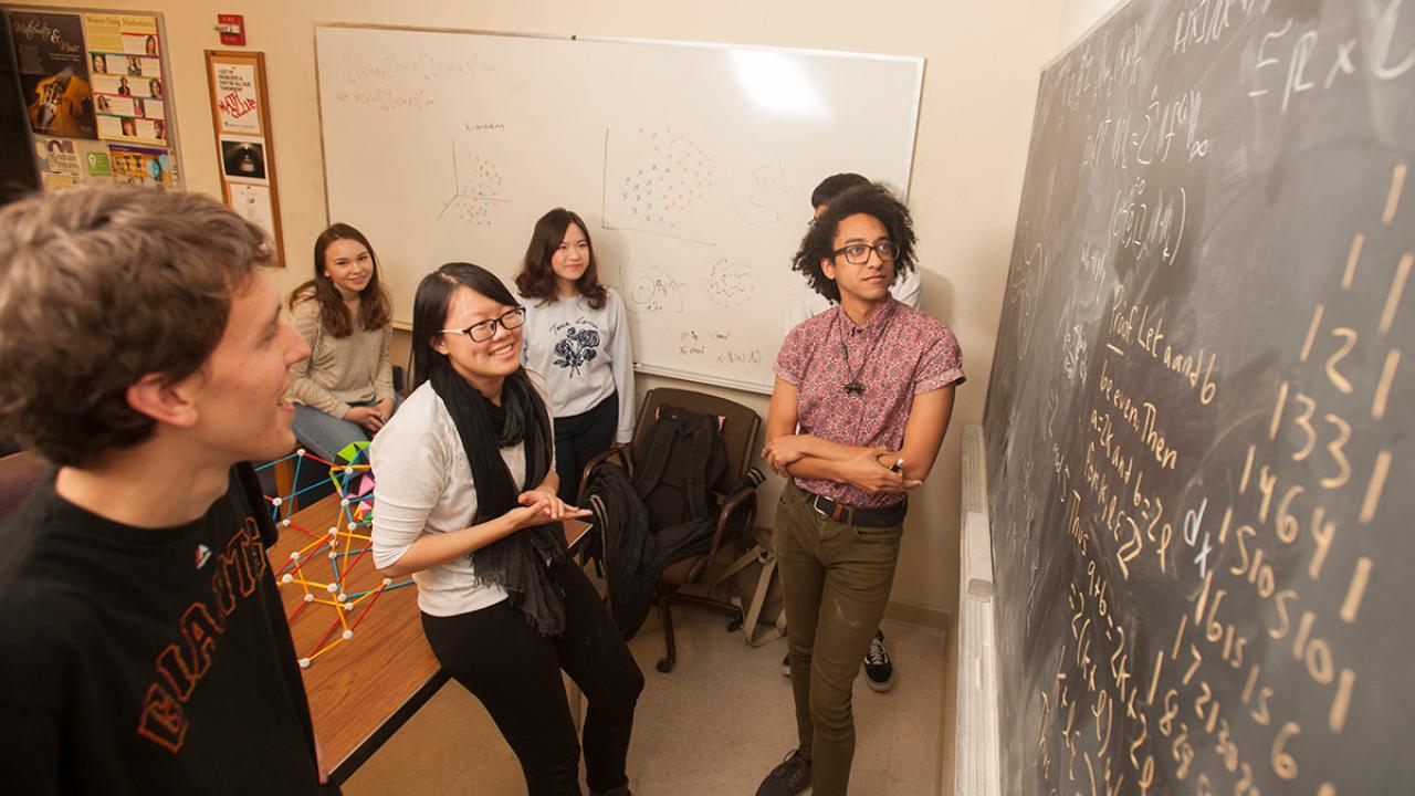 Five male and femal students looking at a blackboard