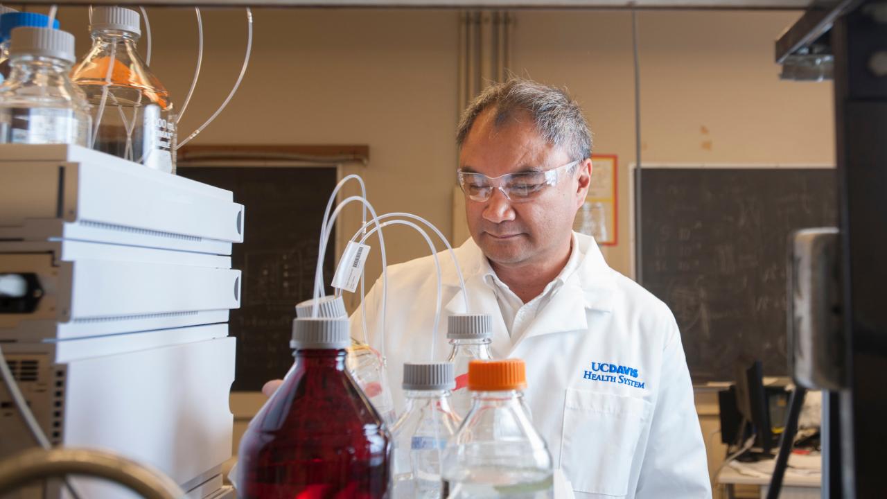 Man with short grey hair wearing a white lab coat working at a lab bench. 