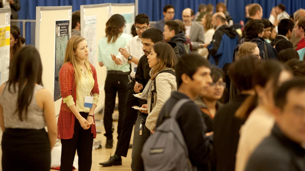 A woman stands in front of a poster and talks with others at a crowded event