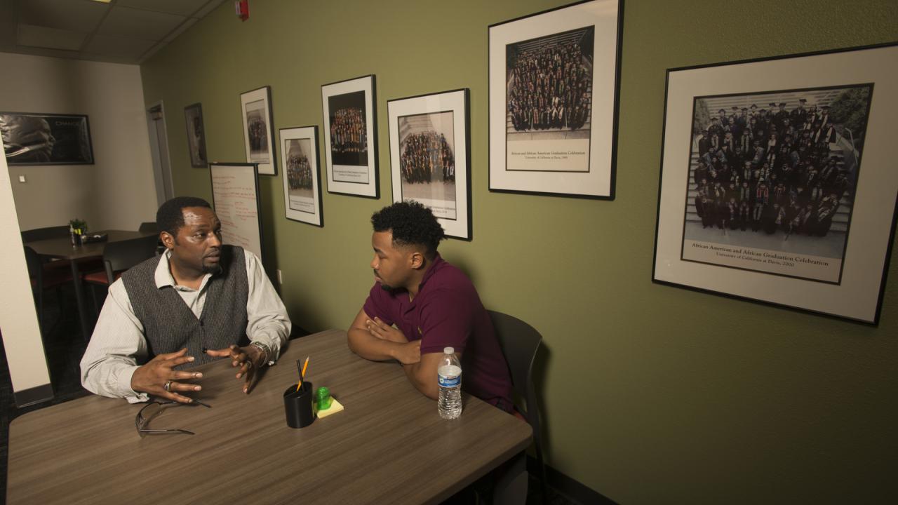 Two men talk at a table