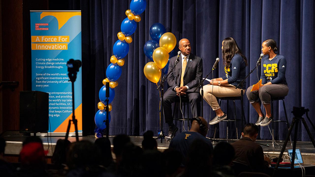 Chancellor Gary S. May at the mike with two students hosting a podcast