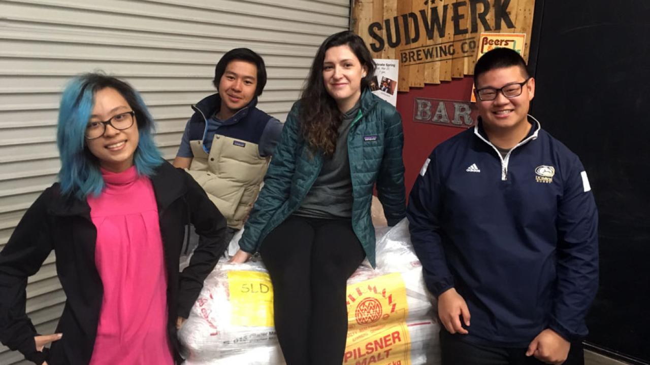 Iron Brew 2017 winning team poses around sacks of malt at Sudwerk Brewing Co.