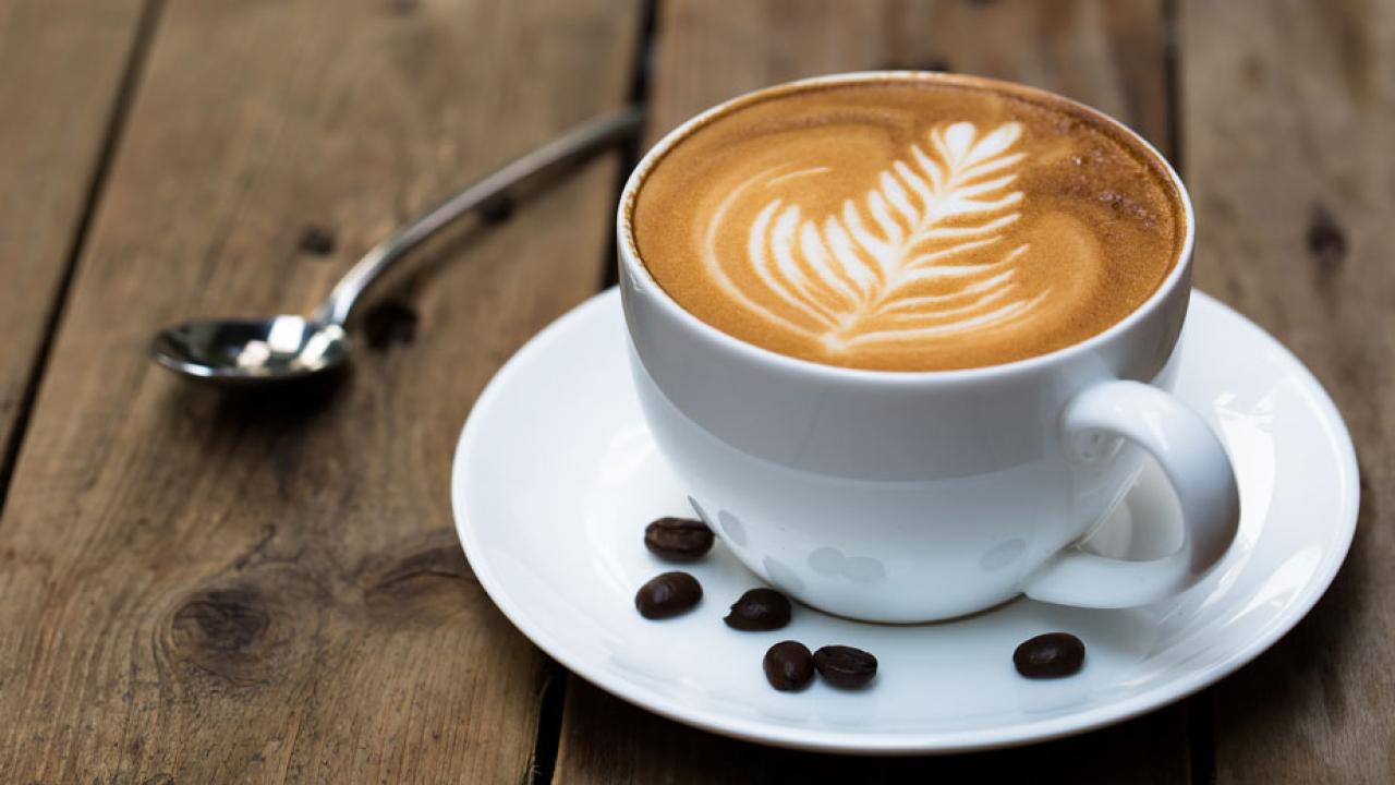 Cup of frothy coffee with design on top, beans in saucercoffee 