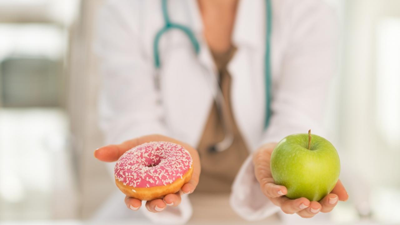 Doctor has doughnut in one hand, apple in the other.