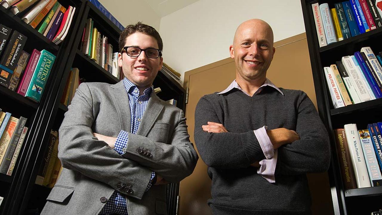 Two men posing in a book-lined office