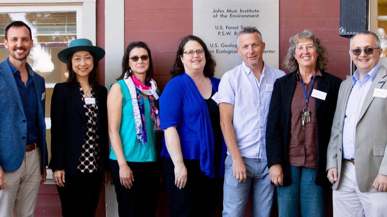 Seven people in a line, for posed picture, outdoors.