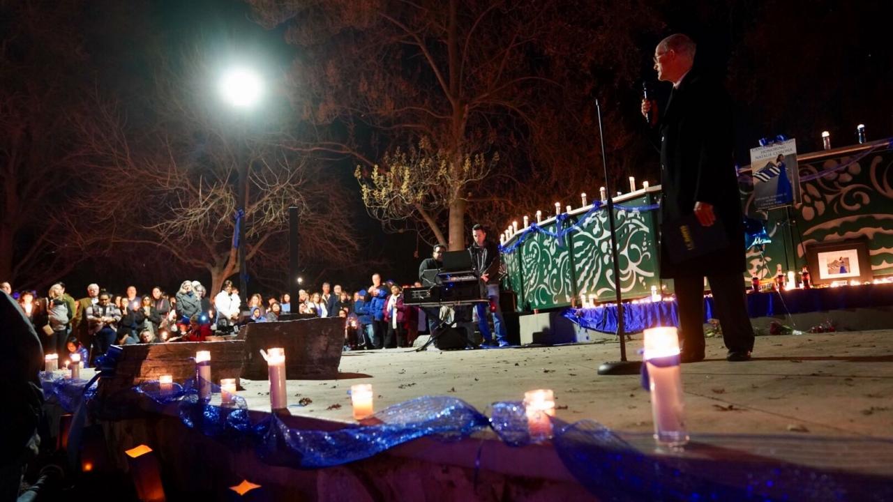 Man talks to audience of people holding candles.