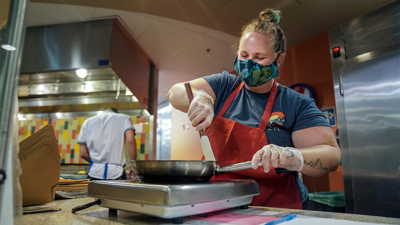 Woman wearing face covering cooks eggs.