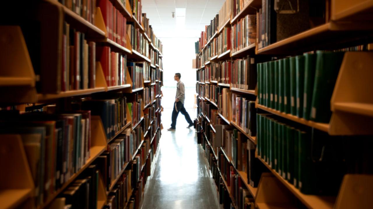 Library stacks, with a patron walking by.