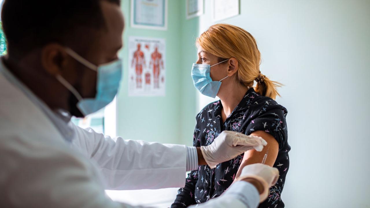 Man administers vaccintaion to woman. Both are wearing masks.