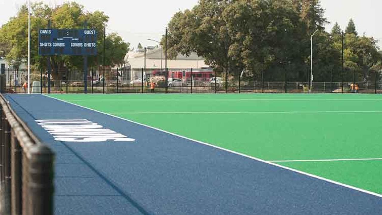 Photo: New field hockey field, showing the artificial turf and blue sideline area, and the scoreboard.
