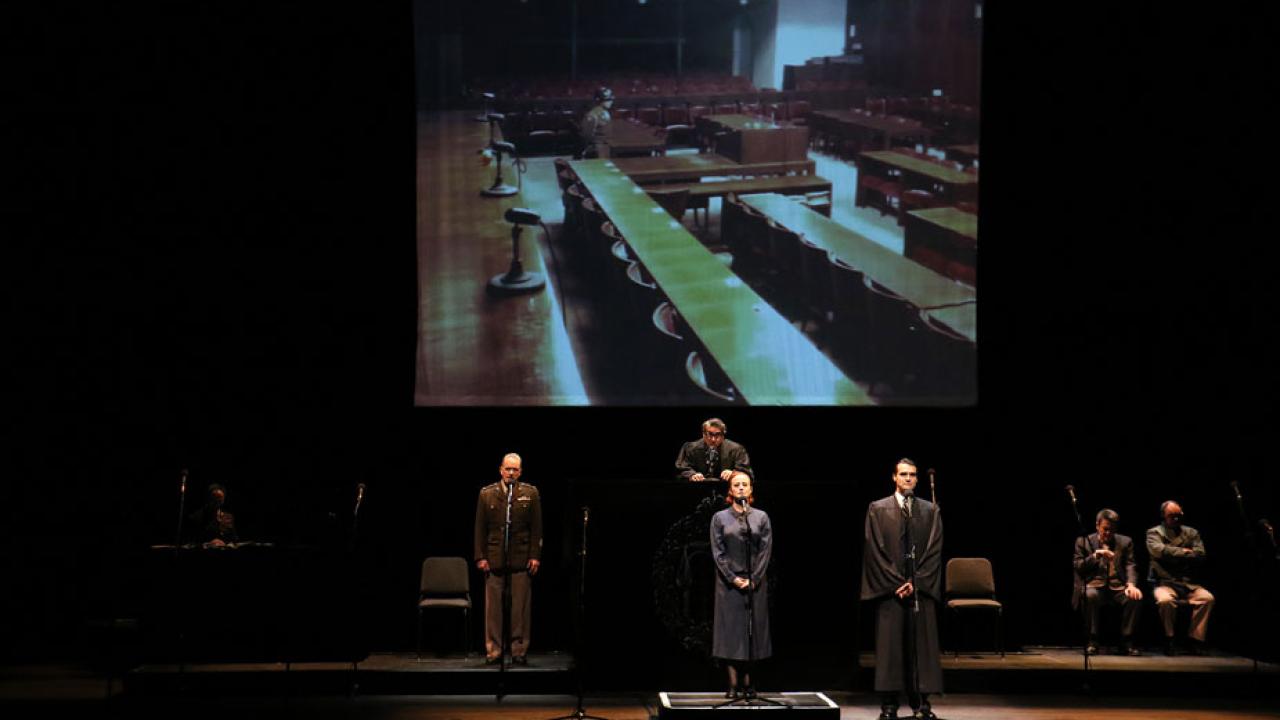 Actors stand before microphones, on stage.