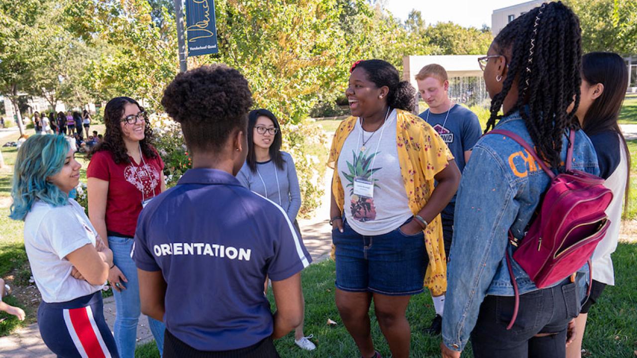 An orientation leader stands with a group of incoming students outdoors.