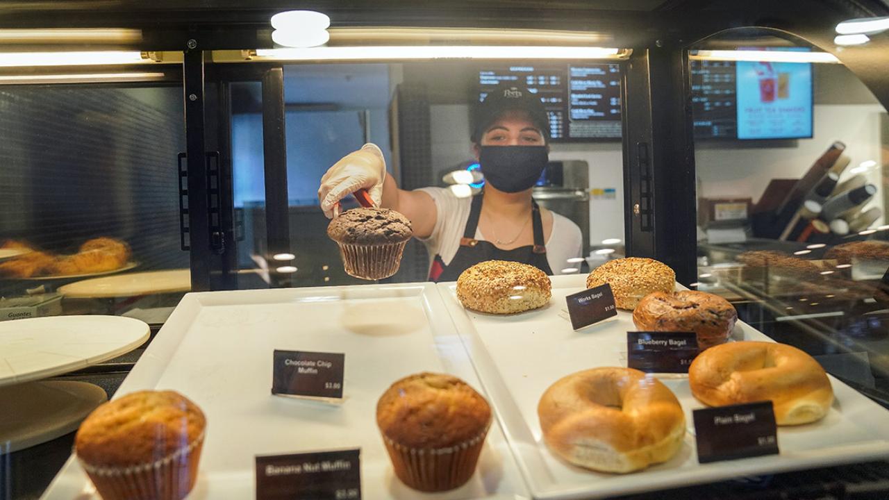 Employee in mask retrieves a pastry from display case.