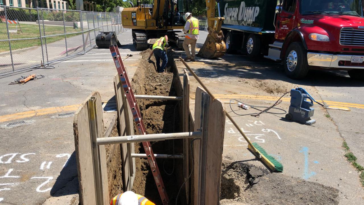 Workers in and around trench in road, for pipeline project.