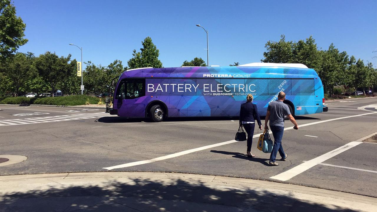 Two people walk through a crosswalk as an electric bus drives by.