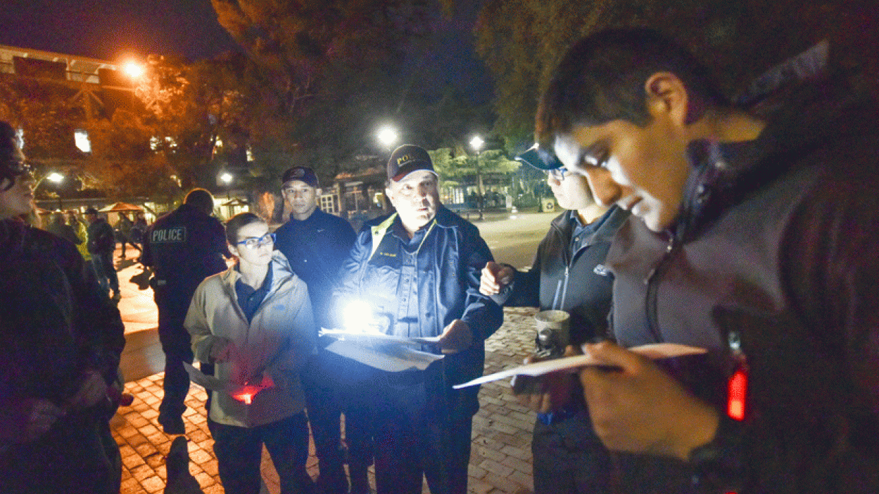 Photo: Police officer surrounded by students, at night, with flashlights, taking notes.