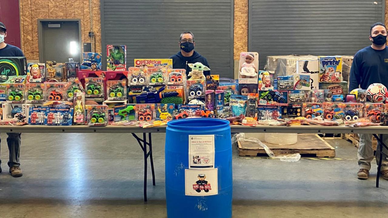 Three man standing behind tables full of toys.