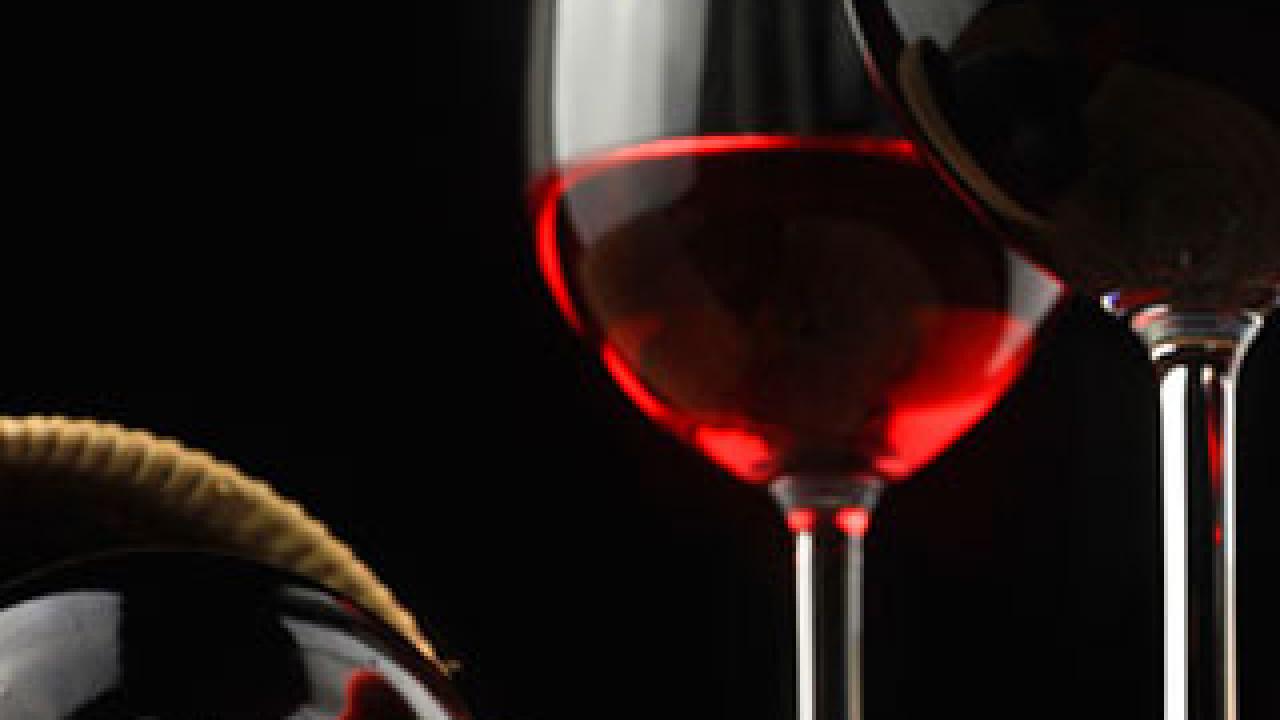 Bottle of wine on its side with a glass of red wine, grapes in the background