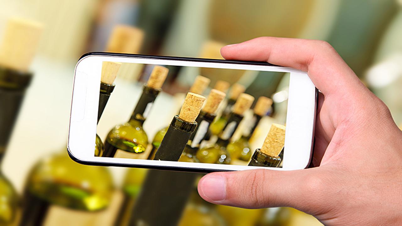 A hand-held cell phone captures an image of wine bottles with corks