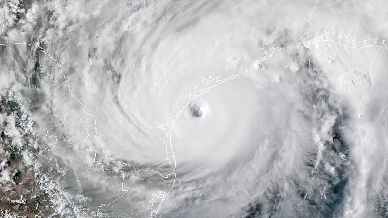 Dense white cloud seen from space spirals outwards from the center of the image. A coastline is barely visible through the cloud. 