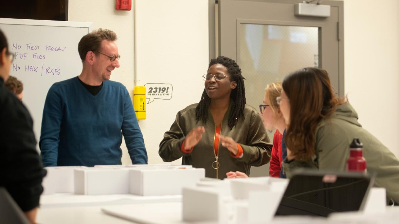 l to r) Professor Tim McNeil listens as Ama Bonsu talks about their layout as Millie Lozano and Zhou Zhou listen during the design exhibition class on February 12, 2019.  The students pick an anniversary in 2019 to showcase and design how the show will work in the Manettie Shrem Musuem.