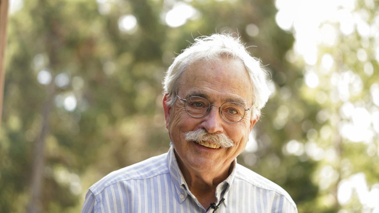 Profile shot of Peter Moyle, smiling in dappled sunlight and tree grove