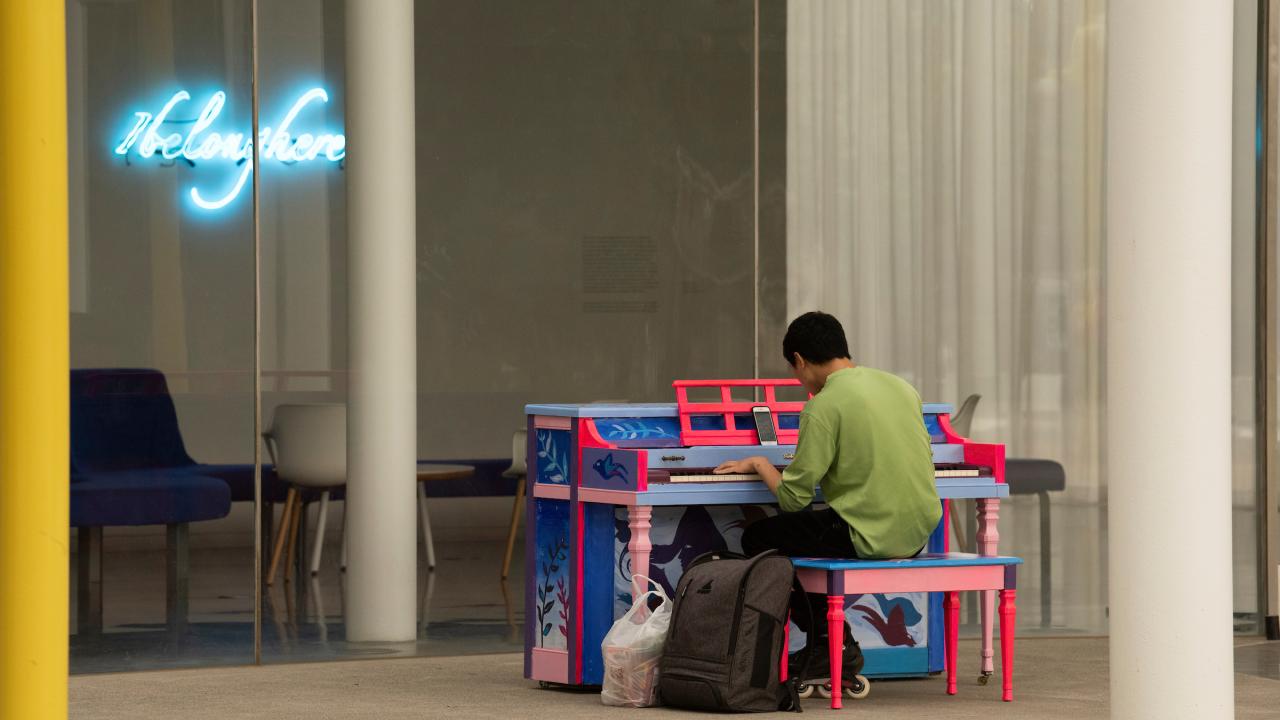 An individual in a green shirt plays the piano outside the Manetti Shrem museum.