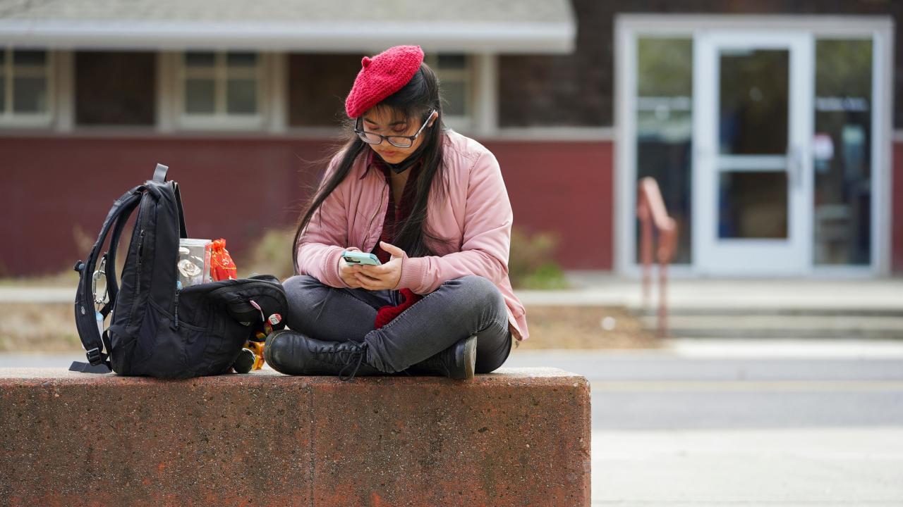 A student in a pink jacket and a red beret uses her smartphone outside of the CRAFT Center on February 14, 2023.