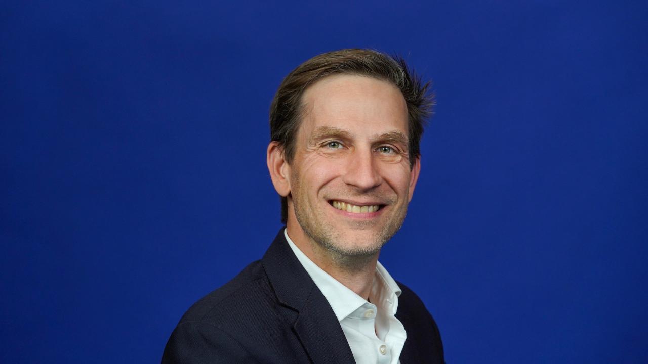 Smiling man in suit, photographic headshot on solid blue background