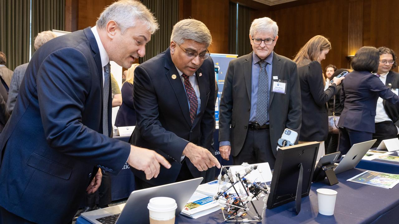 Three men in dark suits looking at gadgets on a table. 