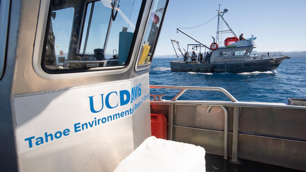 Boat deck with UC Davis Tahoe Environmental logo and a research vessel on a blue lake