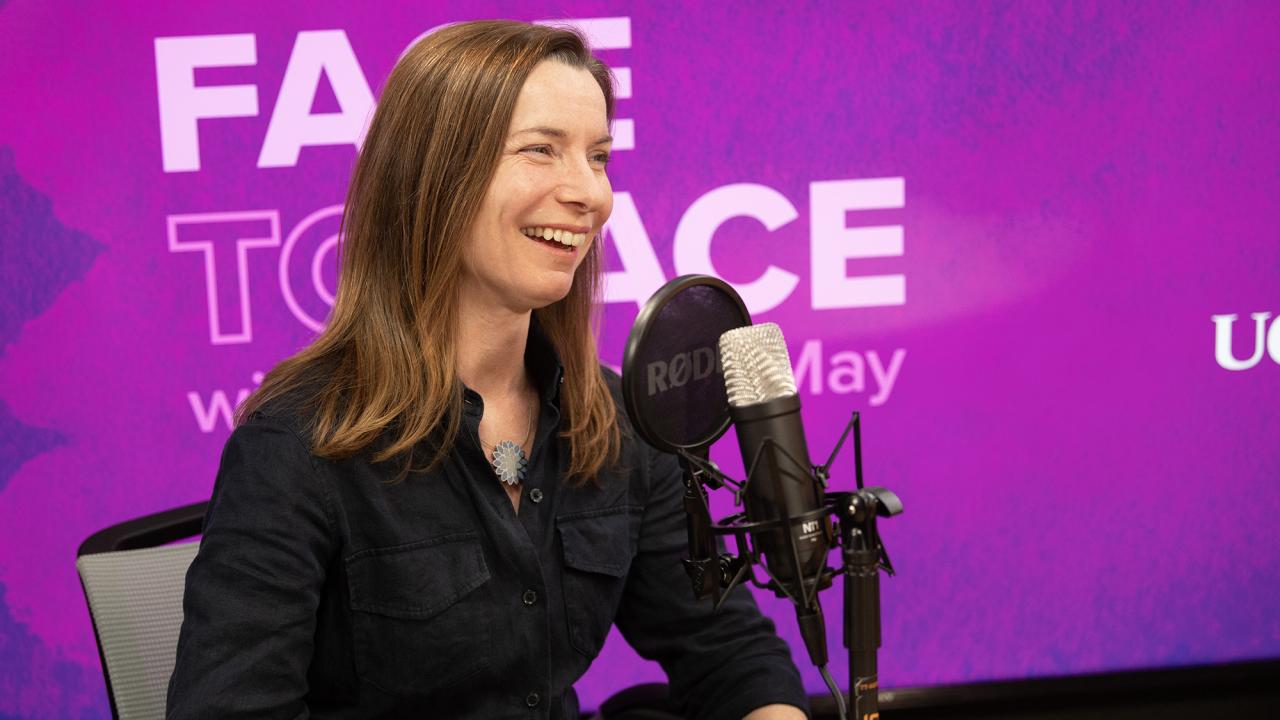 Smiling woman podcast host speaking into a microphone in a purple studio photo